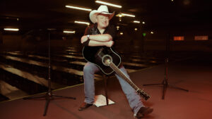 seated man wearing cowboy hat holding acoustic guitar